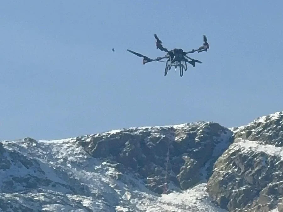 XAG P100 Pro volando con carga suspendida sobre una ladera nevada de la Sierra de Madrid